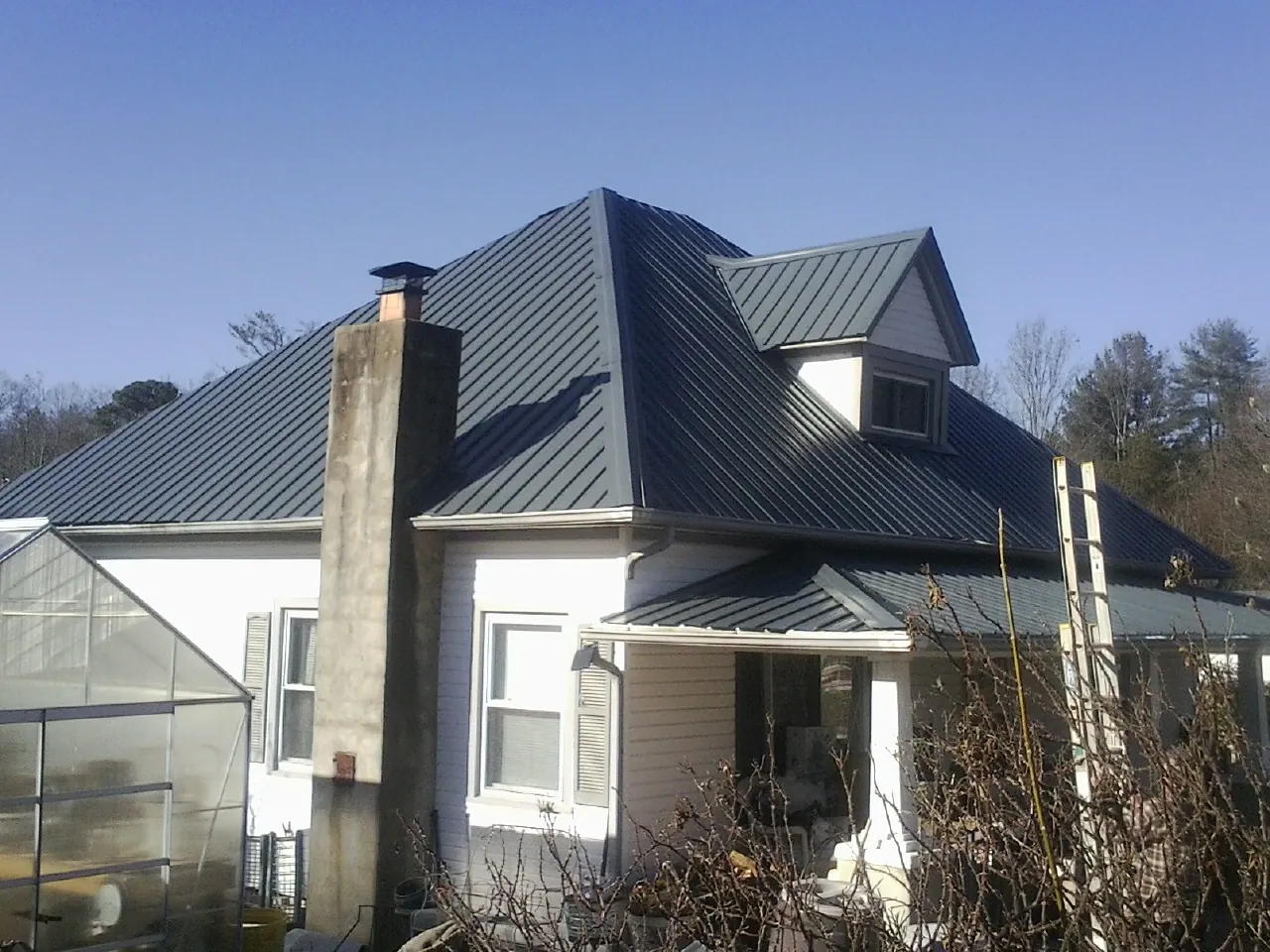Dark blue standing seam metal roof on a white farmhouse with dormer — Slate & Tile Roof Repair by Roofing Brothers in Ocheyedan