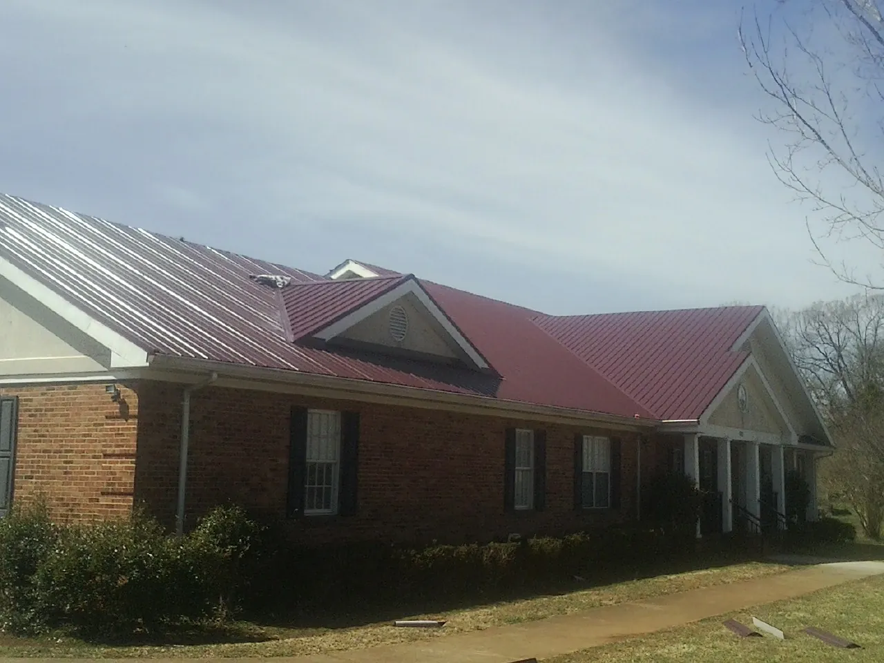 Red metal roof with gabled entries on a long brick building, from a Hail Damage Roof Repair job in Ocheyedan