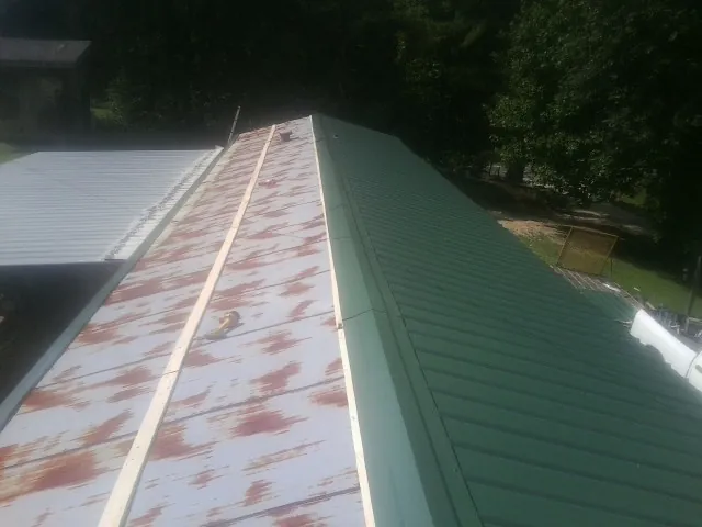 Old rusted panels beside newly installed green metal roofing — Wind Damage Roof Repair by Roofing Brothers in Ocheyedan