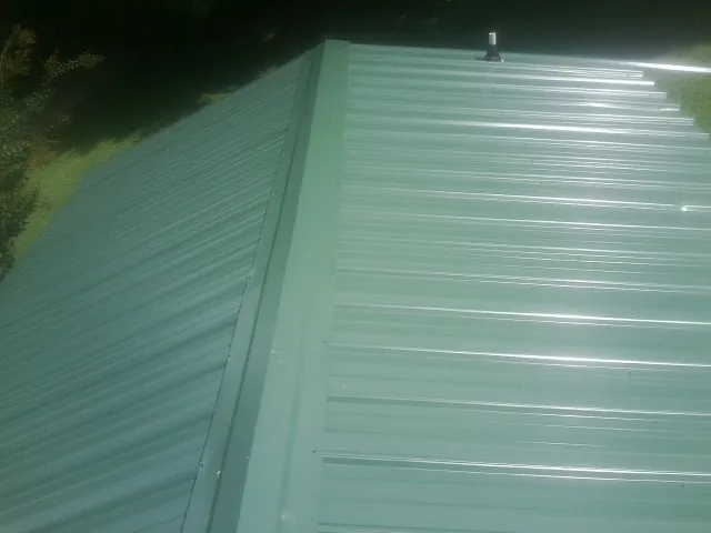 New green metal panels meeting at the ridge of a roof — Flat Roof Repair work by our crew in Ocheyedan