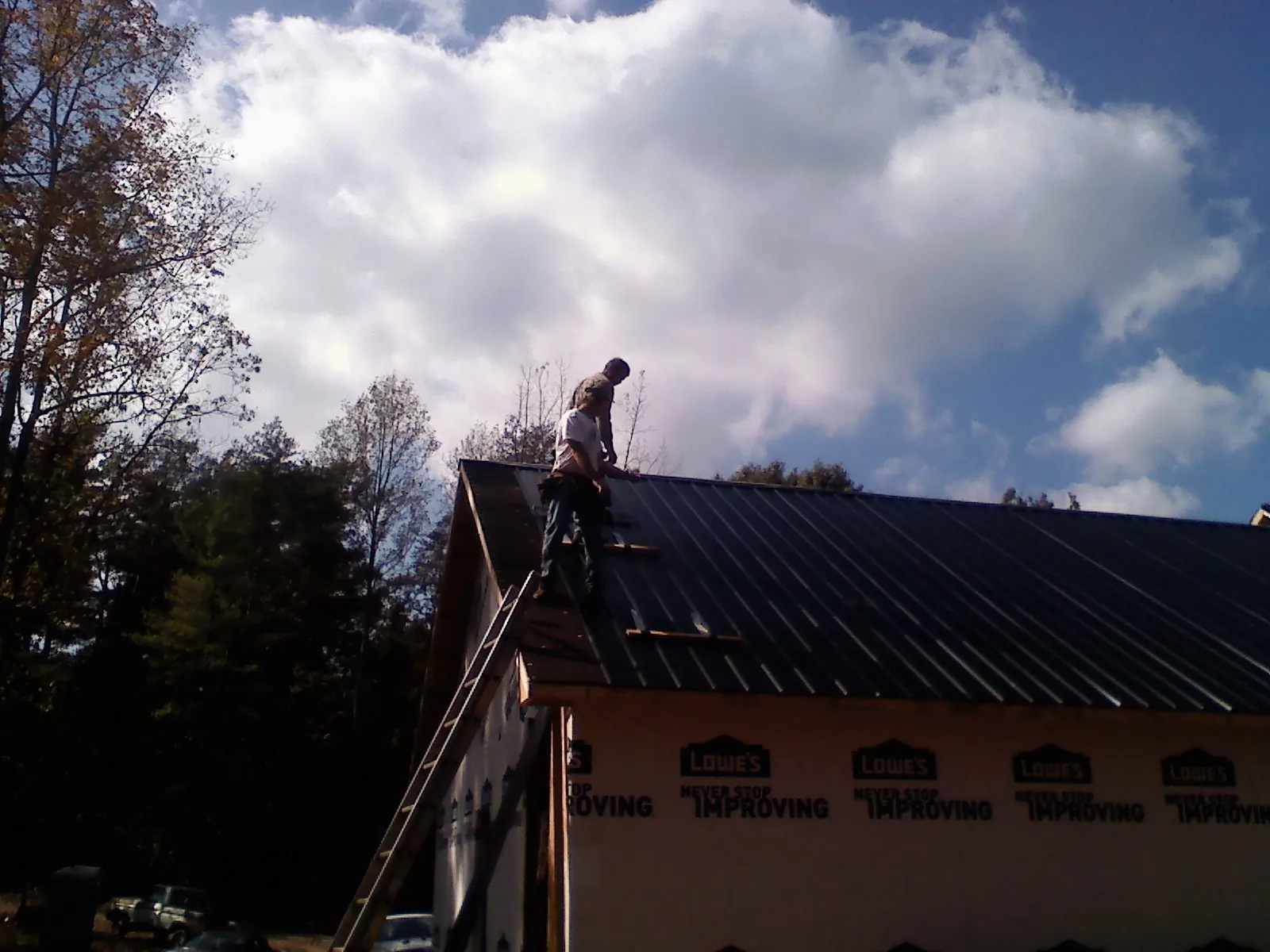 Roofer fastening dark metal panels high against a cloudy sky, from a Roof Inspection job in Ocheyedan