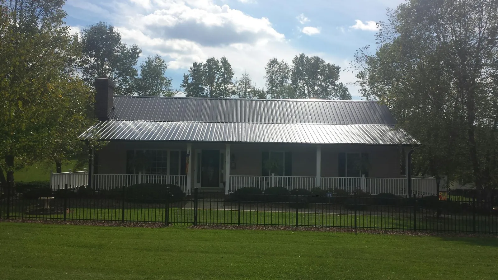 Gray metal roof on a brick ranch with a full width front porch — Gutter Guard Installation work by our crew in Ocheyedan